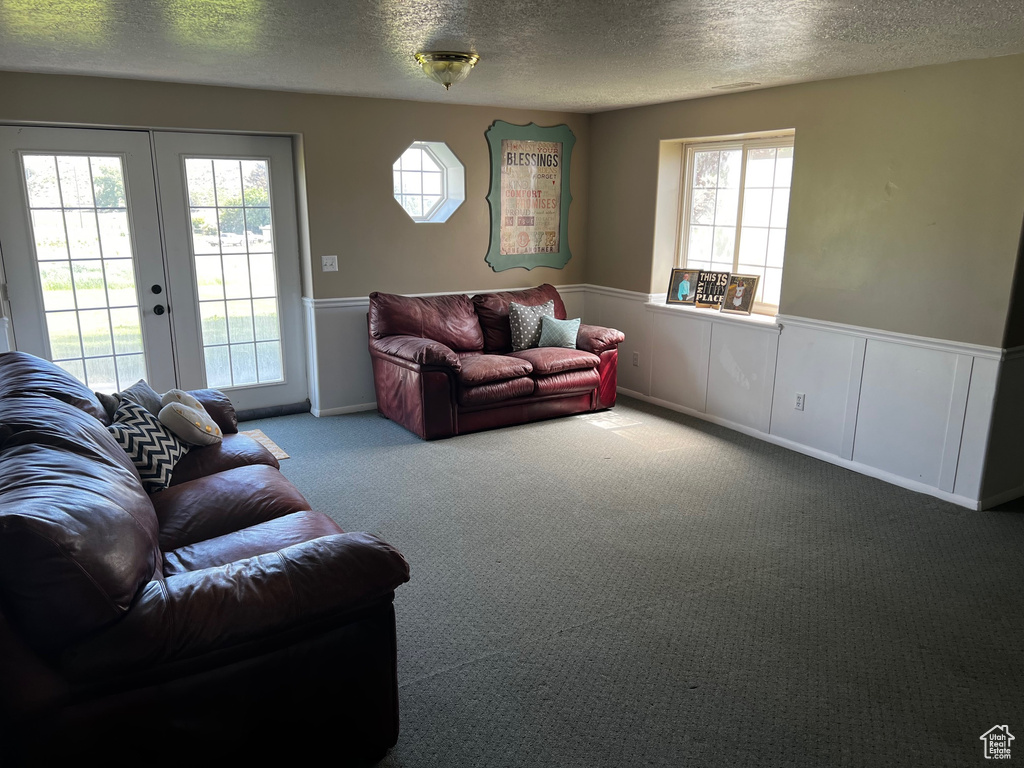 Living room with carpet flooring, a textured ceiling, a wainscoted wall, and french doors