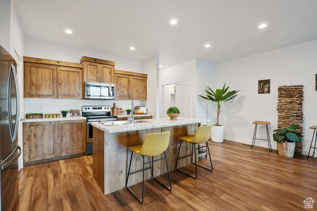 Kitchen featuring appliances with stainless steel finishes, brown cabinetry, a kitchen bar, wood finished floors, and recessed lighting