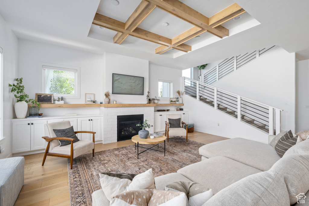 Living area featuring coffered ceiling, light wood-style flooring, stairway, beam ceiling, and a fireplace