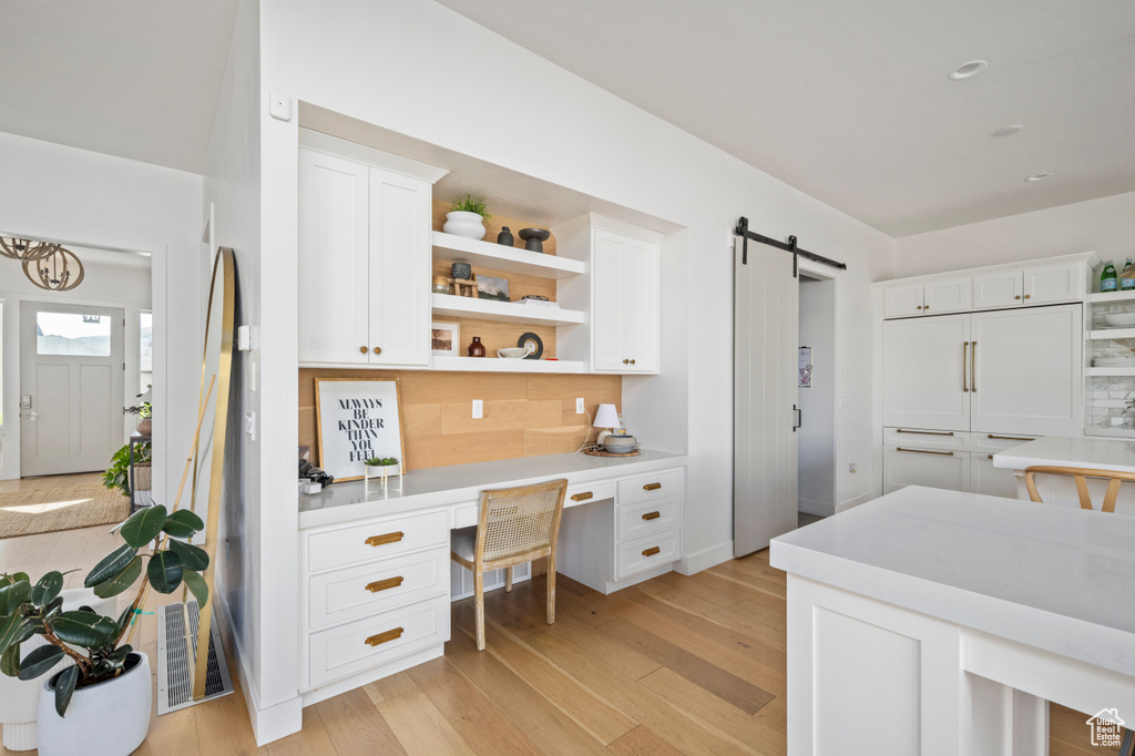 Kitchen with a barn door, backsplash, white cabinets, light countertops, and light wood-style floors