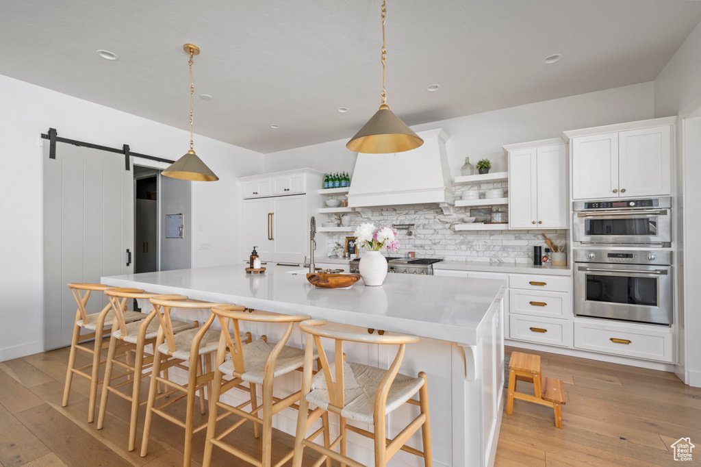 Kitchen featuring open shelves, double oven, decorative backsplash, a barn door, and recessed lighting