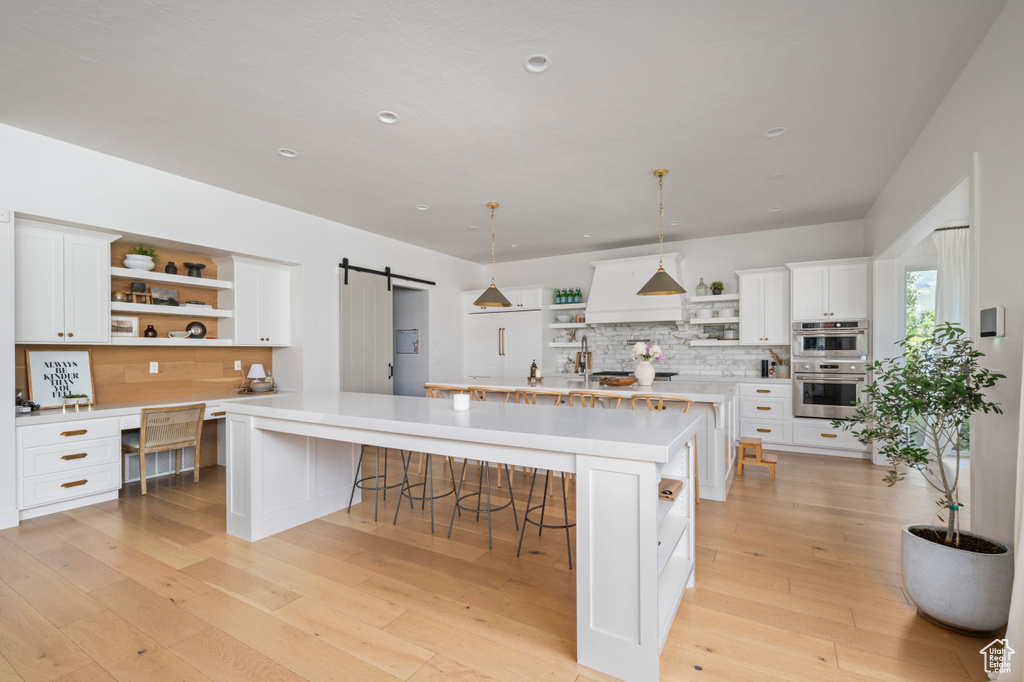 Kitchen with open shelves, a barn door, double oven, light countertops, and backsplash