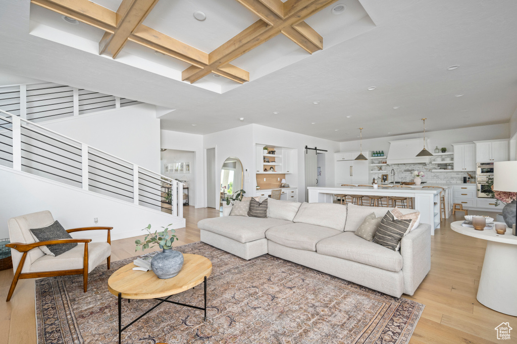 Living area featuring coffered ceiling, a barn door, light wood-type flooring, beamed ceiling, and stairway