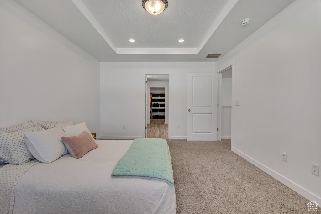 Carpeted bedroom with a tray ceiling, baseboards, a walk in closet, and recessed lighting