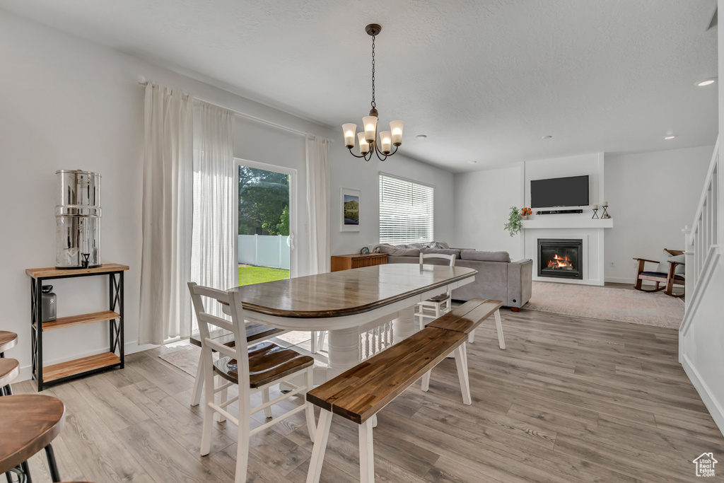 Dining space with light wood-style flooring, a glass covered fireplace, a chandelier, and baseboards