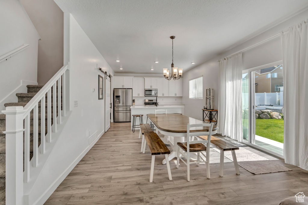 Dining area with a barn door, light wood-style flooring, a chandelier, recessed lighting, and stairway
