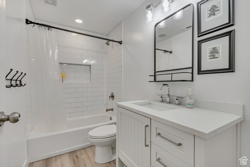 Full bathroom with vanity, shower / tub combo with curtain, wood finished floors, and toilet
