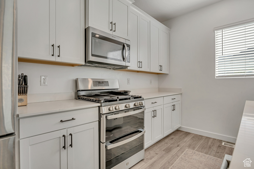 Kitchen featuring appliances with stainless steel finishes, light wood-type flooring, light countertops, white cabinetry, and baseboards