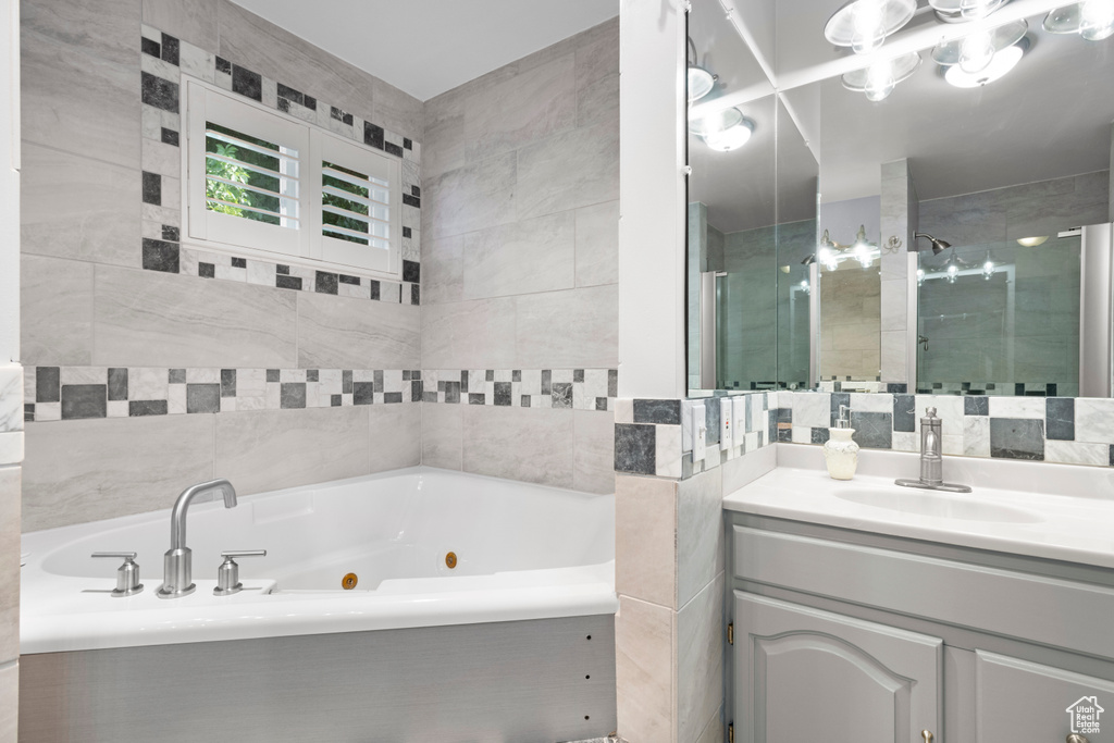Bathroom featuring a tub with jets, vanity, tile walls, and a stall shower