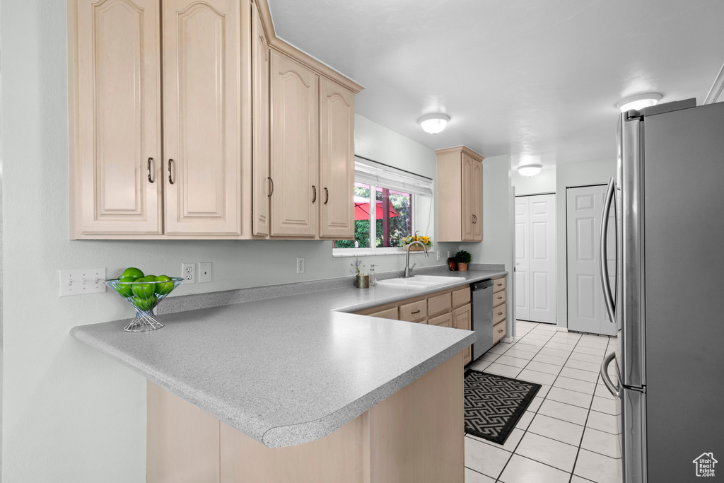 Kitchen with appliances with stainless steel finishes, light brown cabinets, a sink, a peninsula, and light tile patterned floors