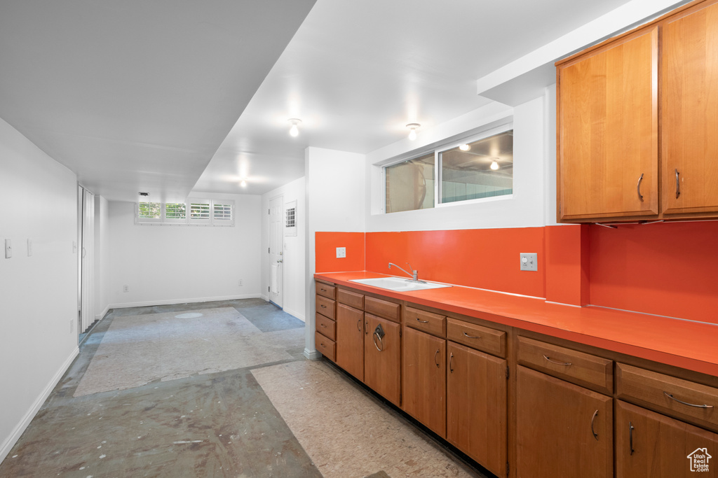 Kitchen with a sink, baseboards, unfinished concrete floors, light countertops, and brown cabinets