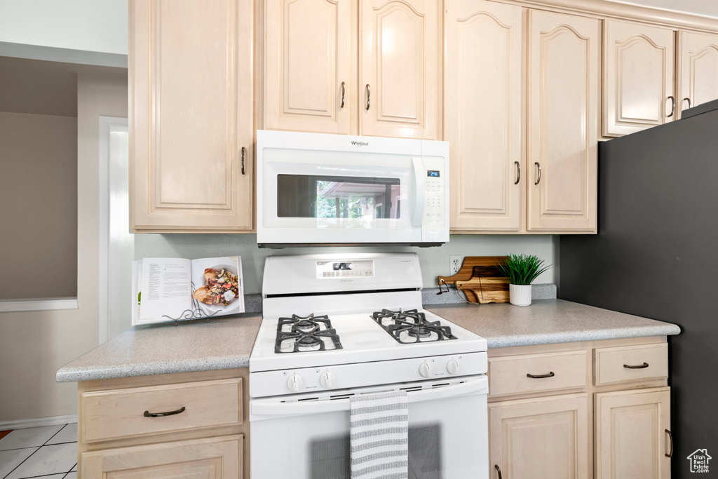 Kitchen with white appliances, light countertops, and light brown cabinetry