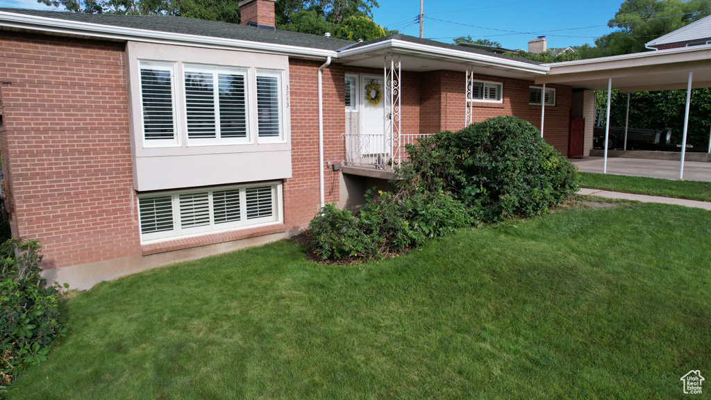 View of front of property with a chimney, brick siding, a front yard, and a carport