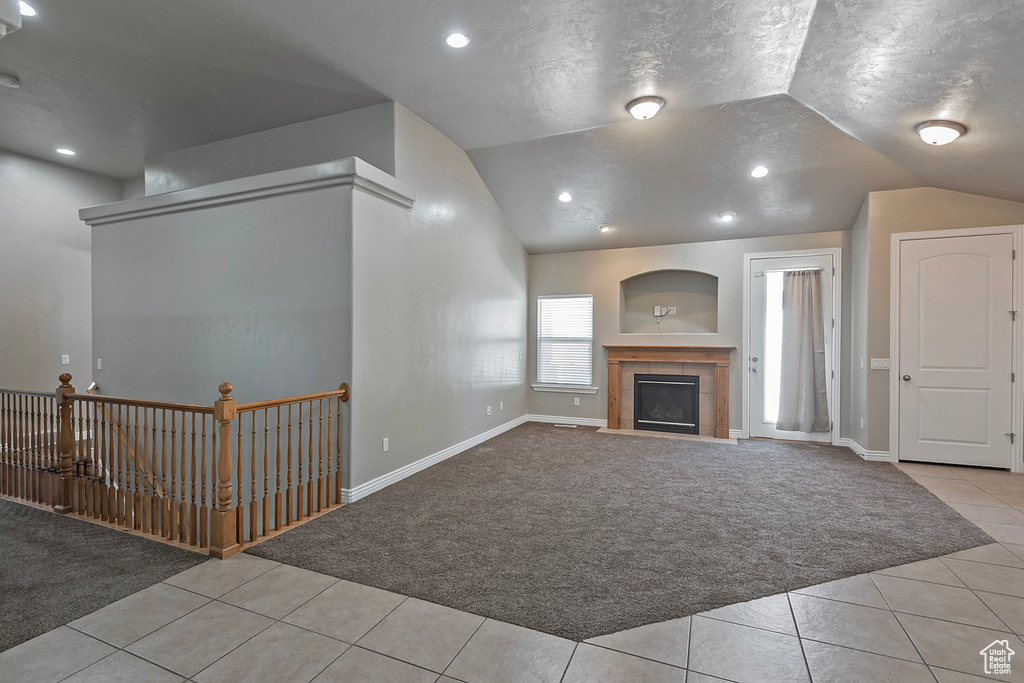 Unfurnished living room with carpet floors, lofted ceiling, tile patterned floors, a tile fireplace, and recessed lighting