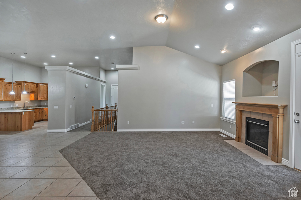 Unfurnished living room featuring lofted ceiling, a fireplace, light tile patterned floors, recessed lighting, and a sink