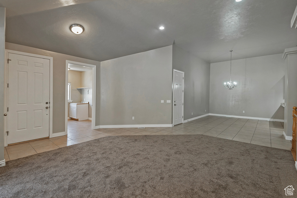 Empty room featuring tile patterned floors, a chandelier, carpet floors, and baseboards