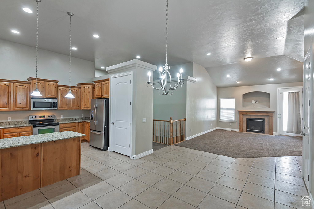 Kitchen with stainless steel appliances, lofted ceiling, light tile patterned flooring, brown cabinetry, and light colored carpet