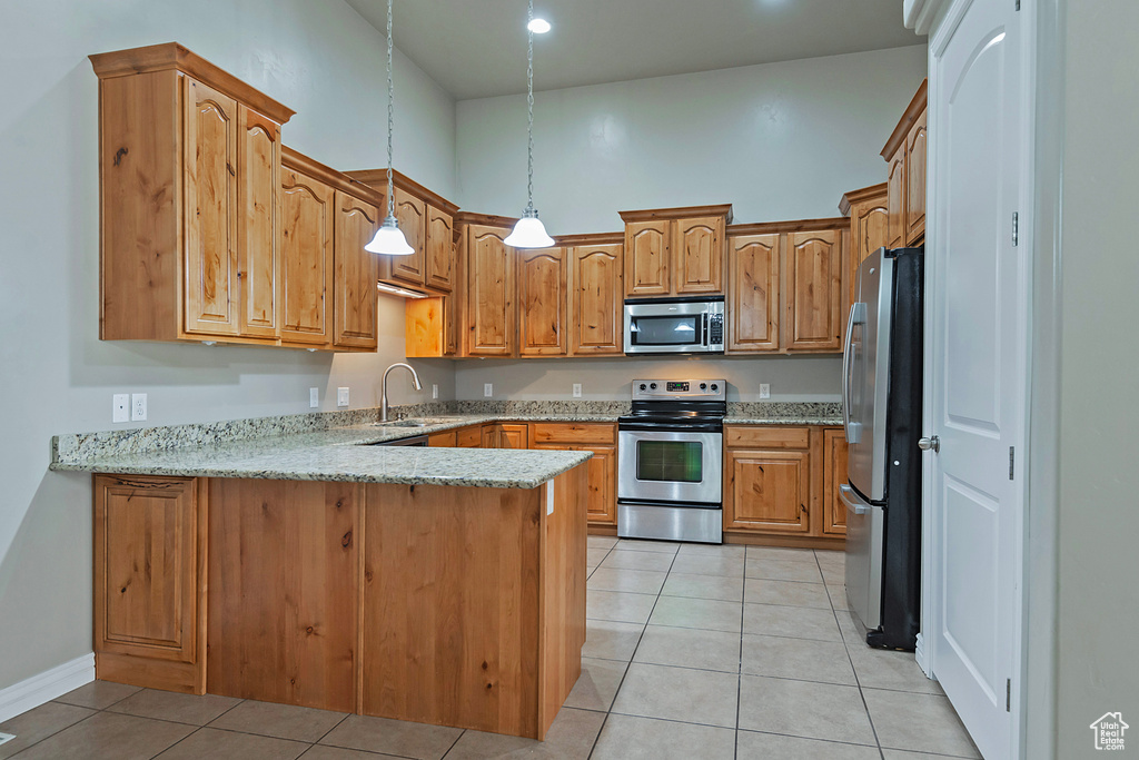 Kitchen with appliances with stainless steel finishes, a peninsula, a sink, light tile patterned floors, and light stone counters