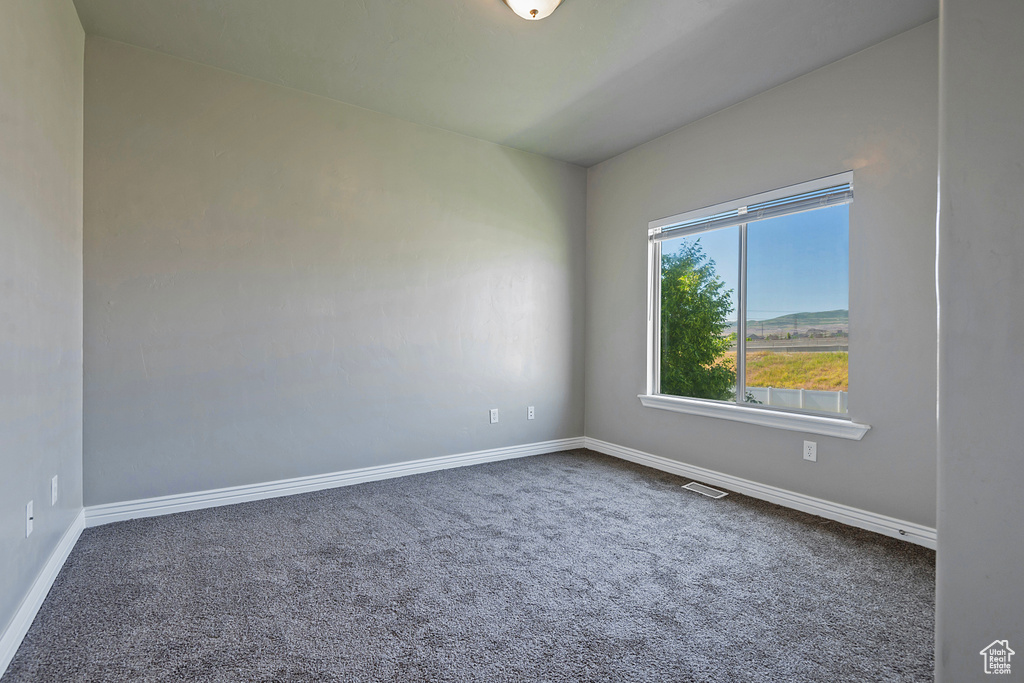 Spare room featuring dark carpet and baseboards