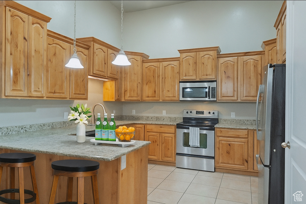 Kitchen featuring stainless steel appliances, light tile patterned flooring, a peninsula, a kitchen breakfast bar, and decorative light fixtures
