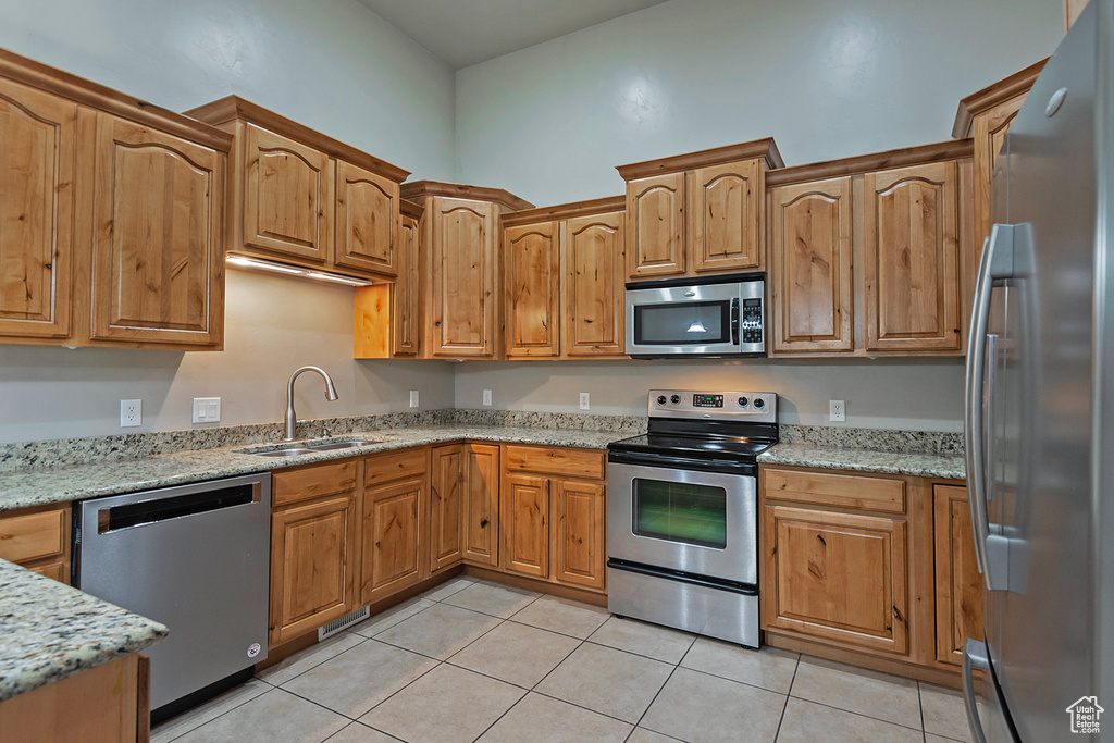 Kitchen featuring appliances with stainless steel finishes, a sink, light tile patterned floors, and light stone countertops