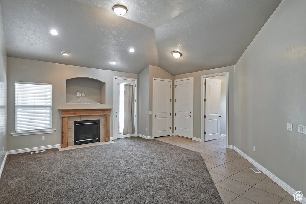 Unfurnished living room featuring light tile patterned flooring, vaulted ceiling, a tiled fireplace, baseboards, and recessed lighting