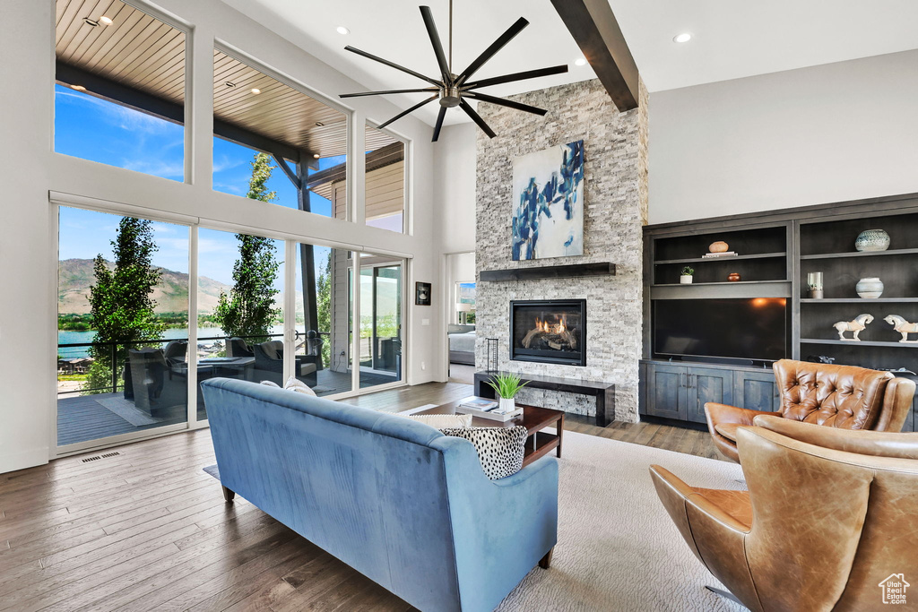 Living area with ceiling fan, a fireplace, hardwood / wood-style flooring, beamed ceiling, and a towering ceiling