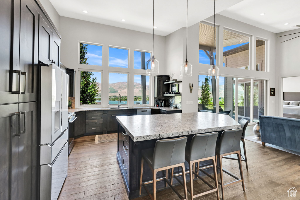 Kitchen featuring a high ceiling, stainless steel appliances, light wood-type flooring, a kitchen island, and a sink