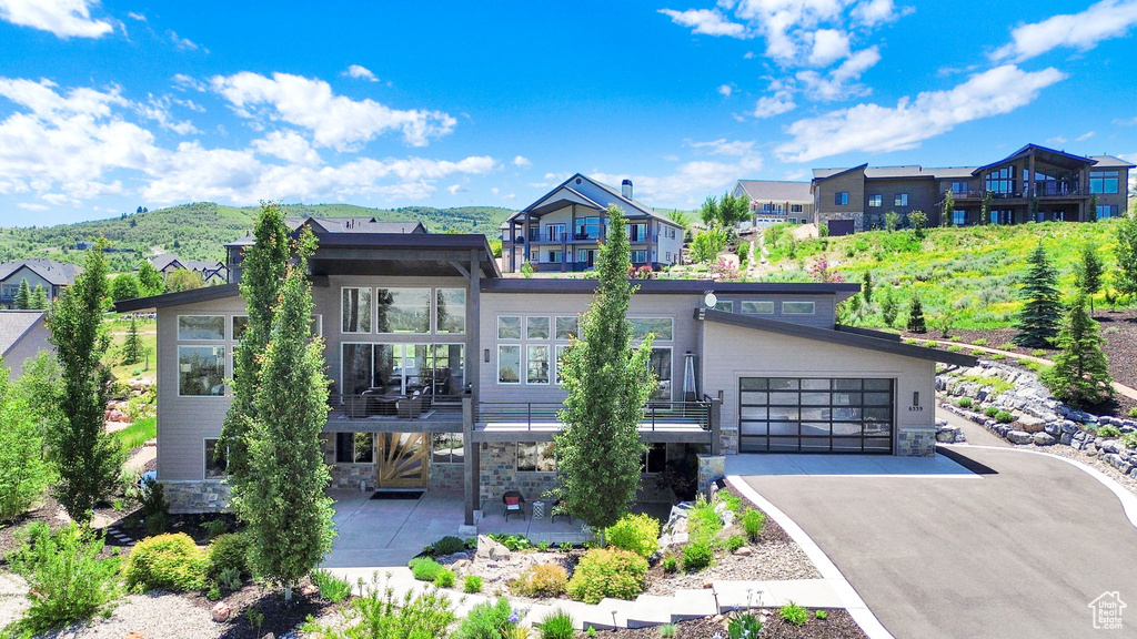 Contemporary home featuring stone siding, driveway, a patio area, a garage, and a balcony