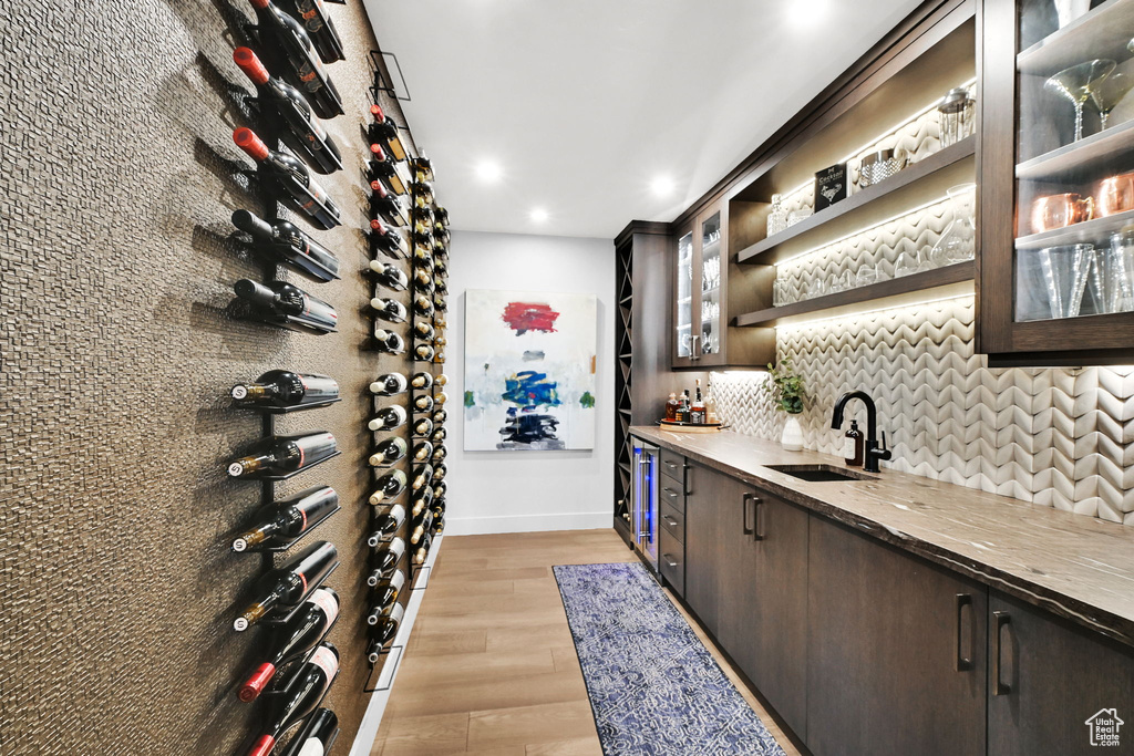 Wine cellar featuring bar with sink, light wood-style floors, recessed lighting, baseboards, and wine cooler
