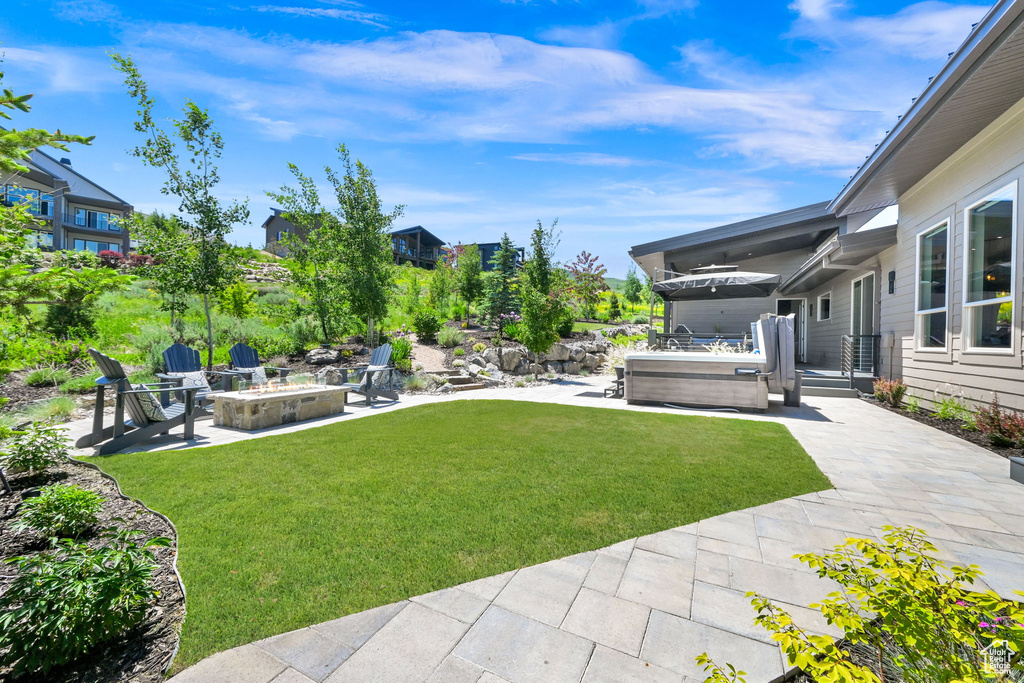 View of green lawn featuring a patio area, an outdoor fire pit, and a hot tub
