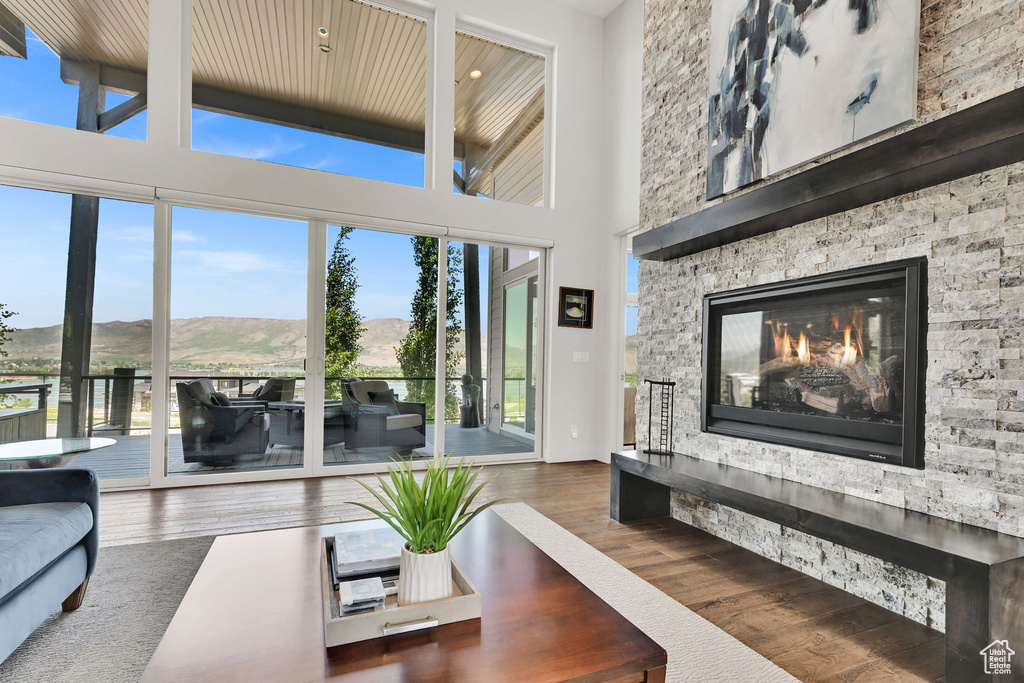Living room featuring wood finished floors, plenty of natural light, a stone fireplace, a mountain view, and a high ceiling
