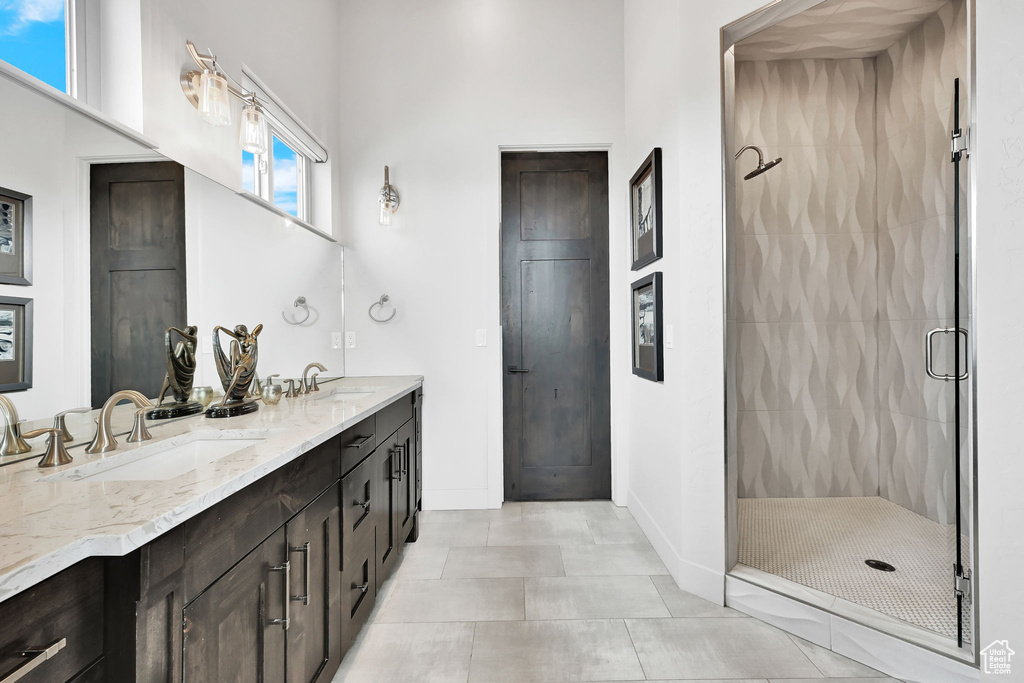 Bathroom featuring a shower stall, double vanity, baseboards, and tile patterned flooring