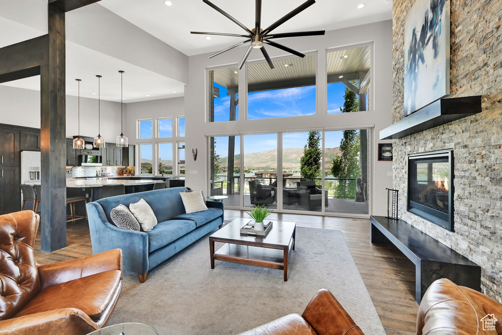 Living room featuring ceiling fan, a towering ceiling, wood finished floors, a stone fireplace, and recessed lighting