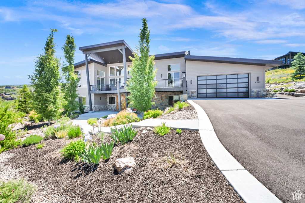 Contemporary home with asphalt driveway, an attached garage, stone siding, and a balcony
