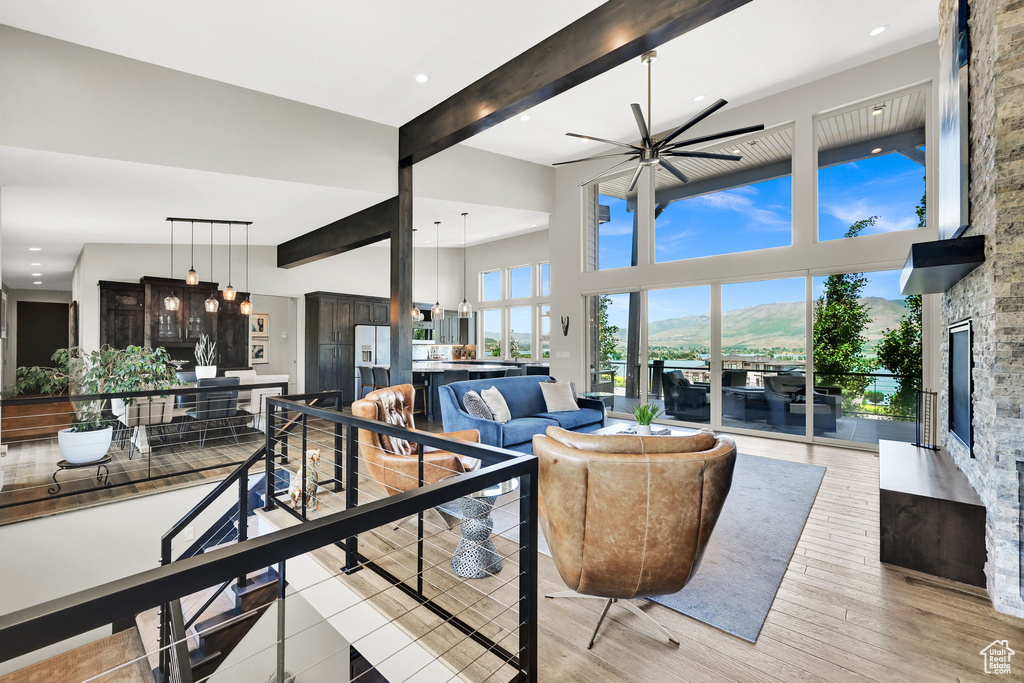 Living room featuring a fireplace, beamed ceiling, a high ceiling, ceiling fan, and light wood-style flooring