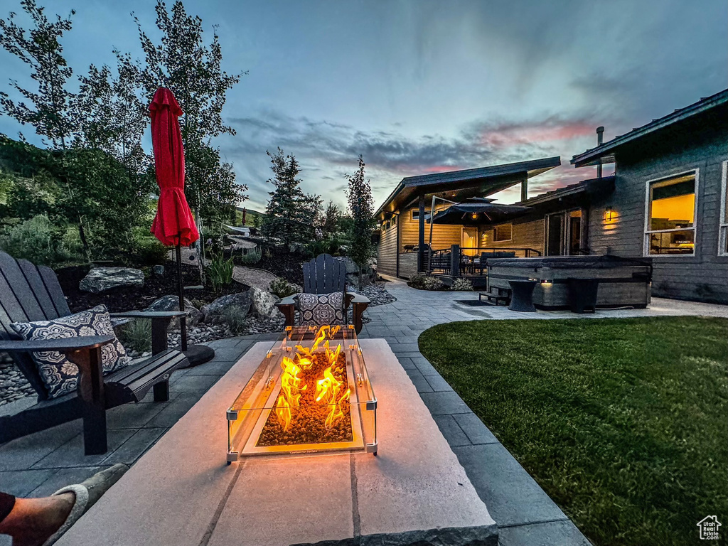 Patio terrace at dusk featuring a hot tub, a fire pit, a patio area, and a lawn