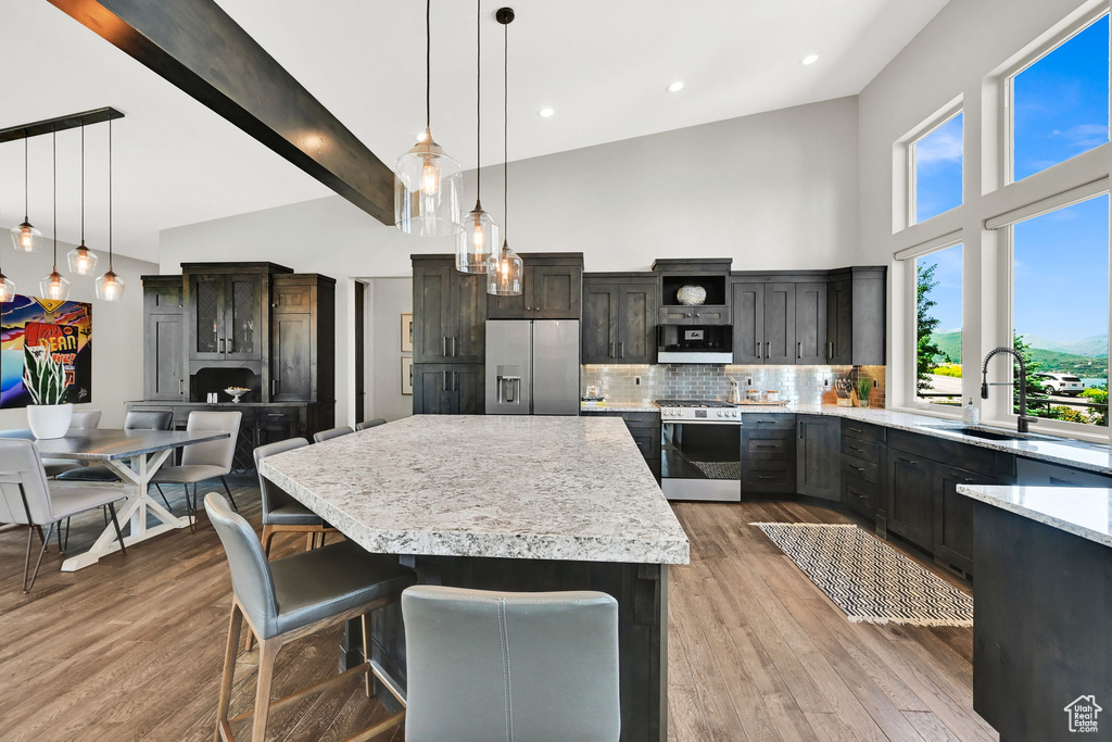 Kitchen featuring stainless steel appliances, high vaulted ceiling, light countertops, a center island, and tasteful backsplash