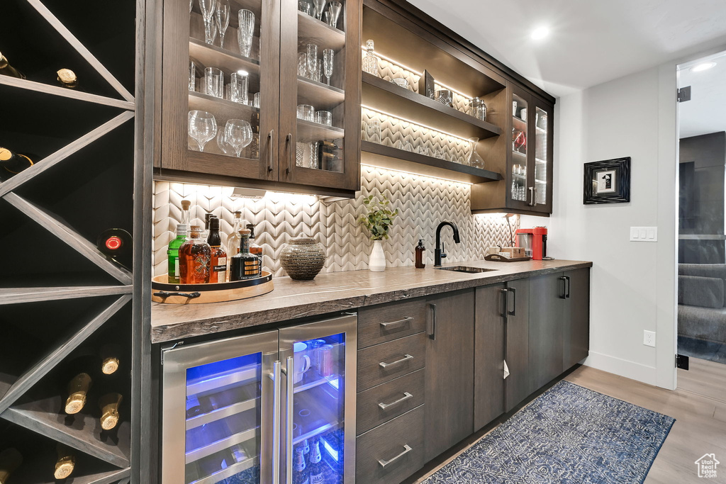 Indoor wet bar featuring beverage cooler, backsplash, light wood-style flooring, and baseboards