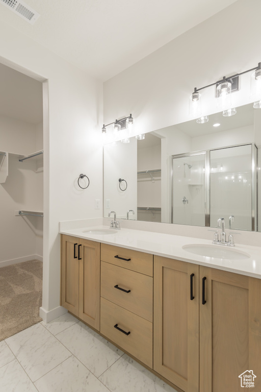 Bathroom with a walk in closet, double vanity, a stall shower, baseboards, and marble look tile flooring