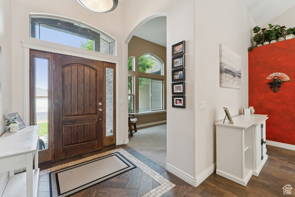 Foyer entrance featuring baseboards, arched walkways, dark wood-style flooring, and a high ceiling