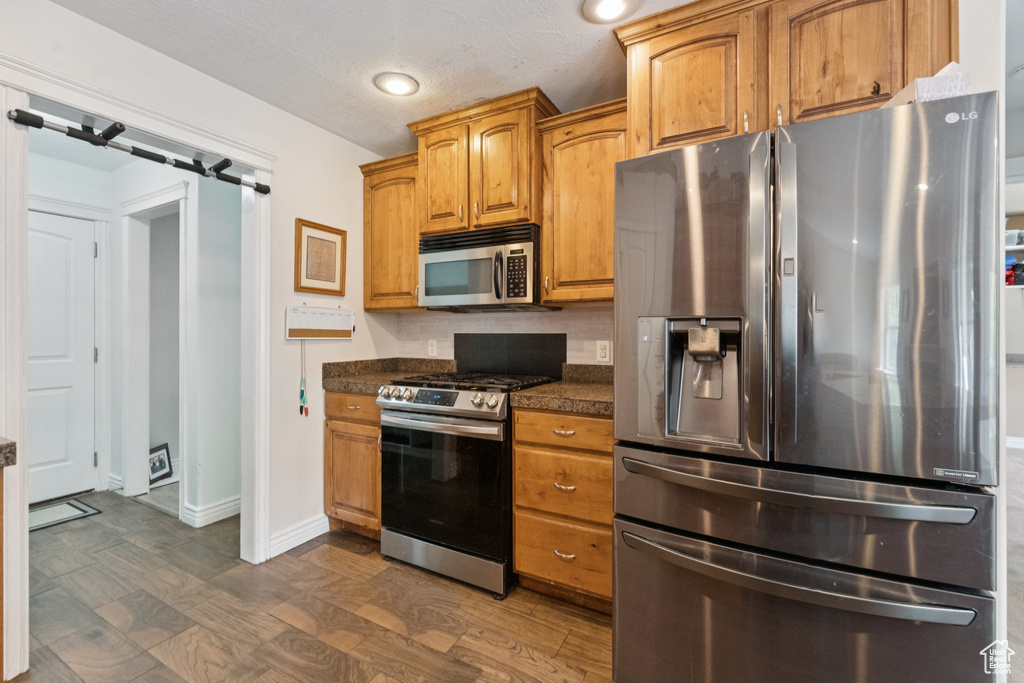 Kitchen with stainless steel appliances, dark countertops, baseboards, brown cabinets, and recessed lighting