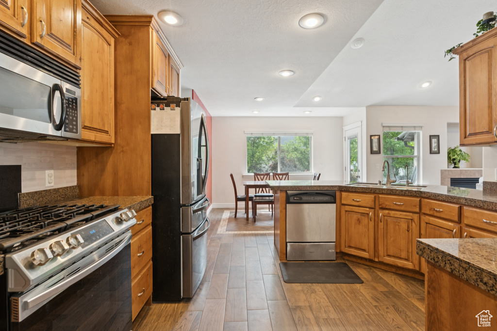 Kitchen featuring stainless steel appliances, brown cabinets, wood finished floors, and recessed lighting