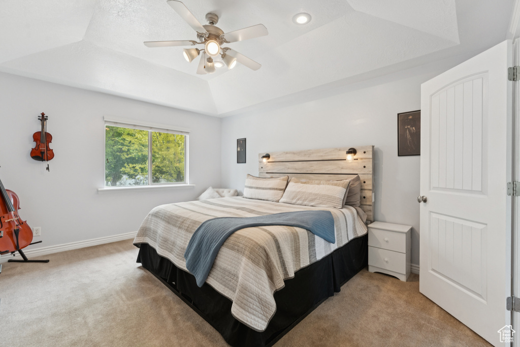 Bedroom with light carpet, a raised ceiling, a ceiling fan, and baseboards