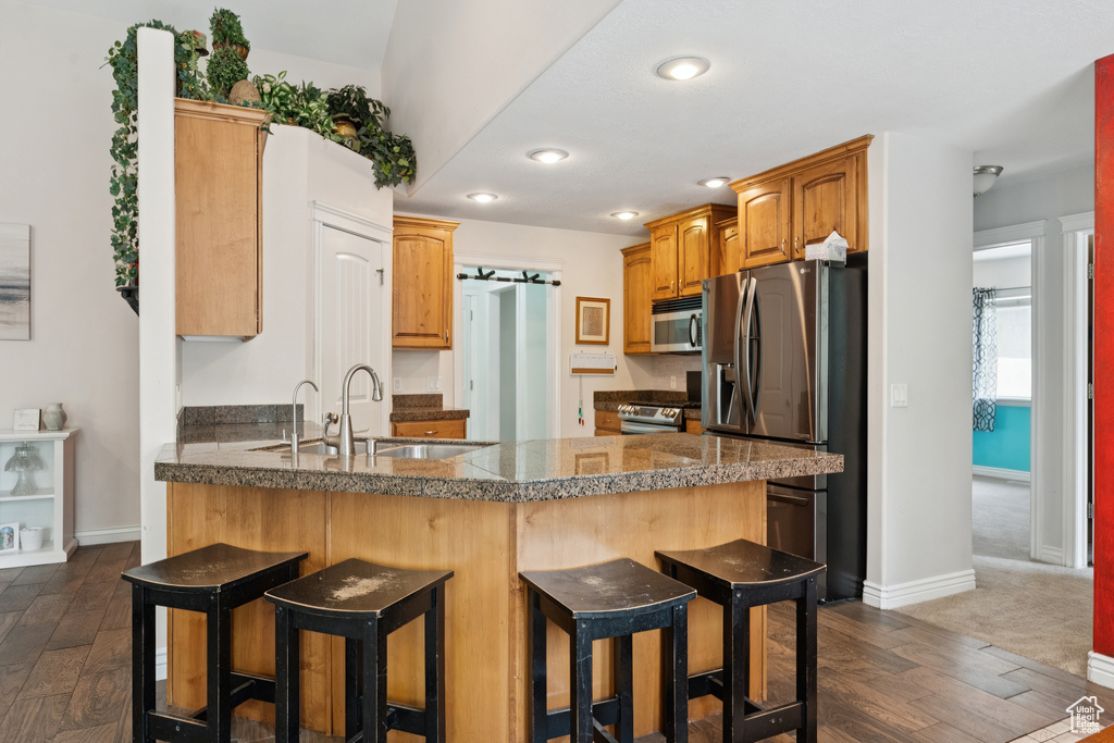 Kitchen with stainless steel appliances, a peninsula, a sink, tile counters, and a breakfast bar area