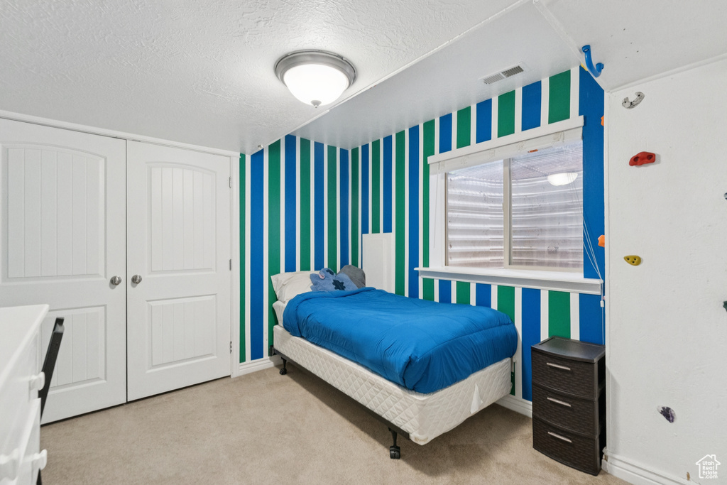 Carpeted bedroom with wallpapered walls, a closet, and a textured ceiling