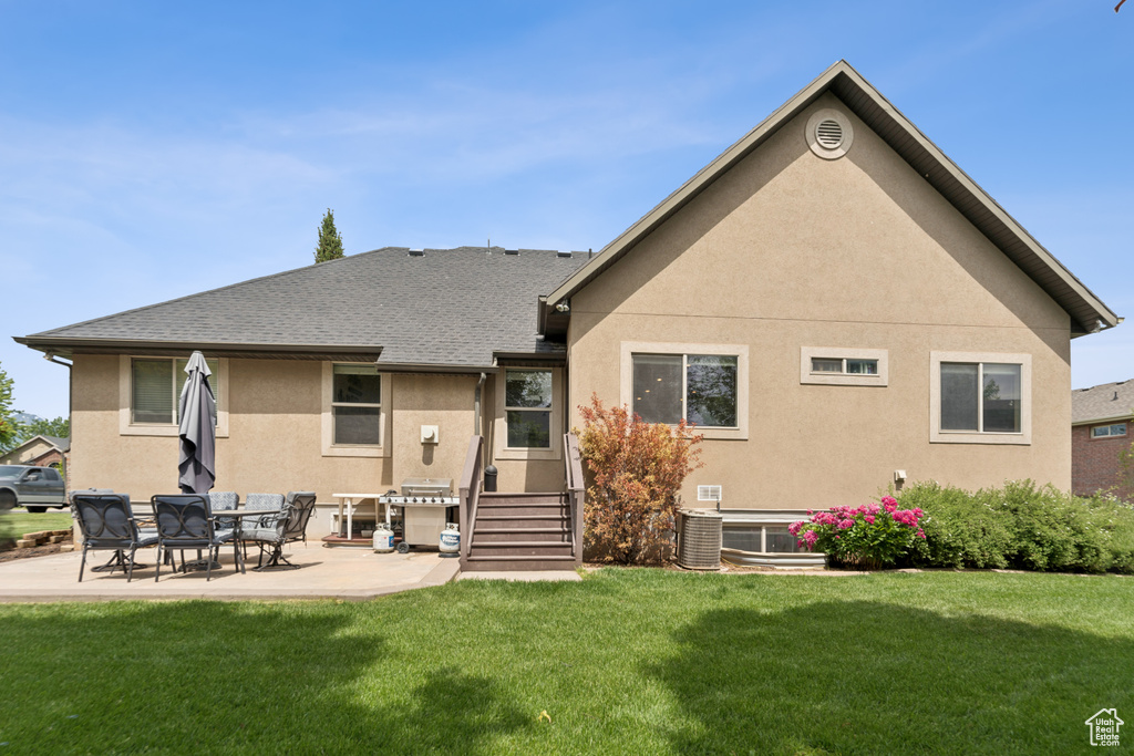 Rear view of property featuring stucco siding, a lawn, a patio, and roof with shingles