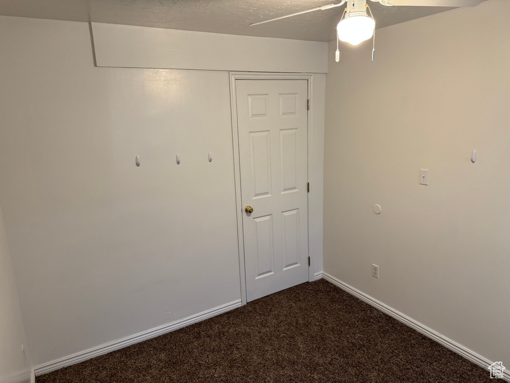 Empty room with dark carpet, ceiling fan, and baseboards