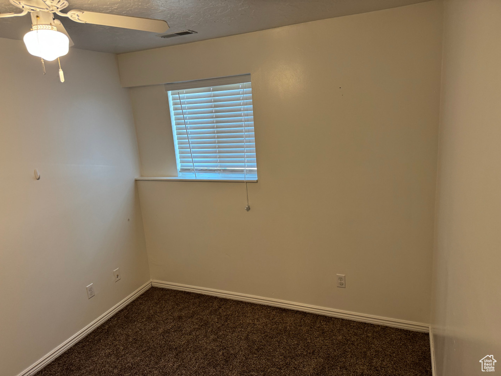 Spare room with dark colored carpet, a ceiling fan, and baseboards