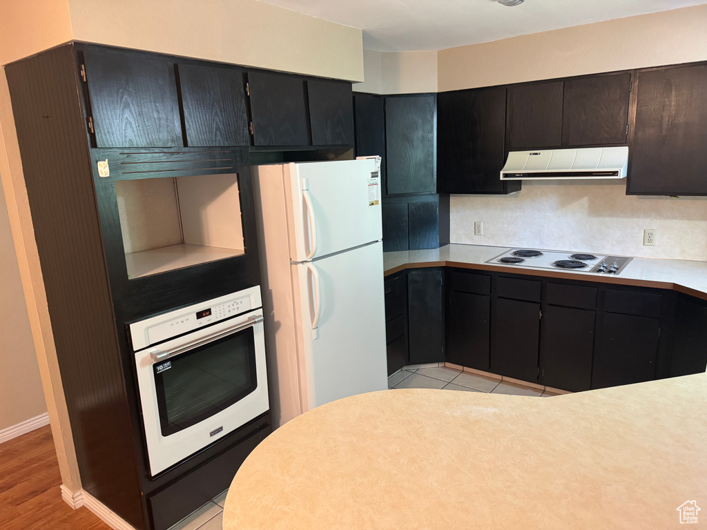 Kitchen featuring white appliances, exhaust hood, light countertops, light wood-style floors, and baseboards